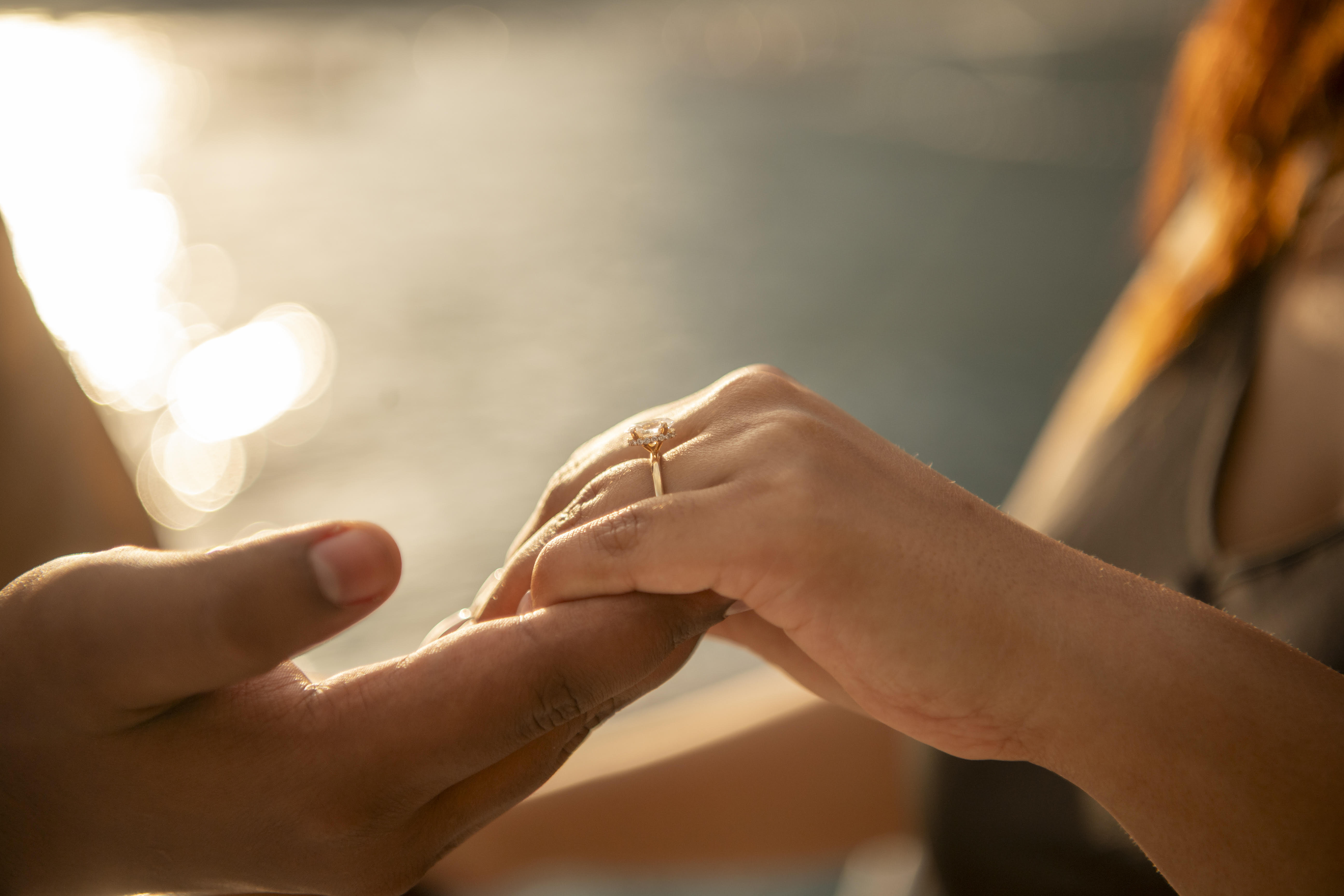 Close-up of hands reaching toward each other in golden sunlight, showing the engagement ring